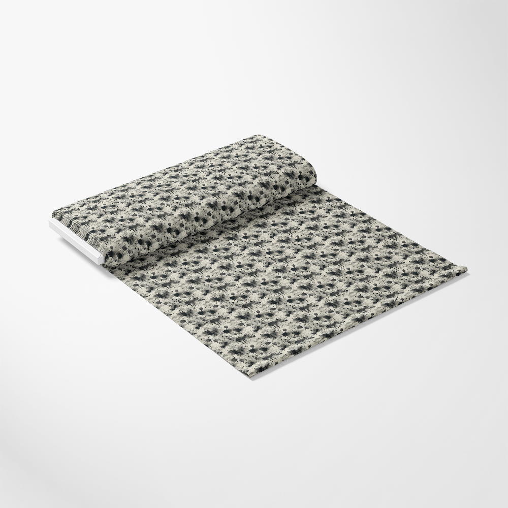 A roll of fabric partially unrolled on a white surface, featuring a repeating black and gray floral pattern.
