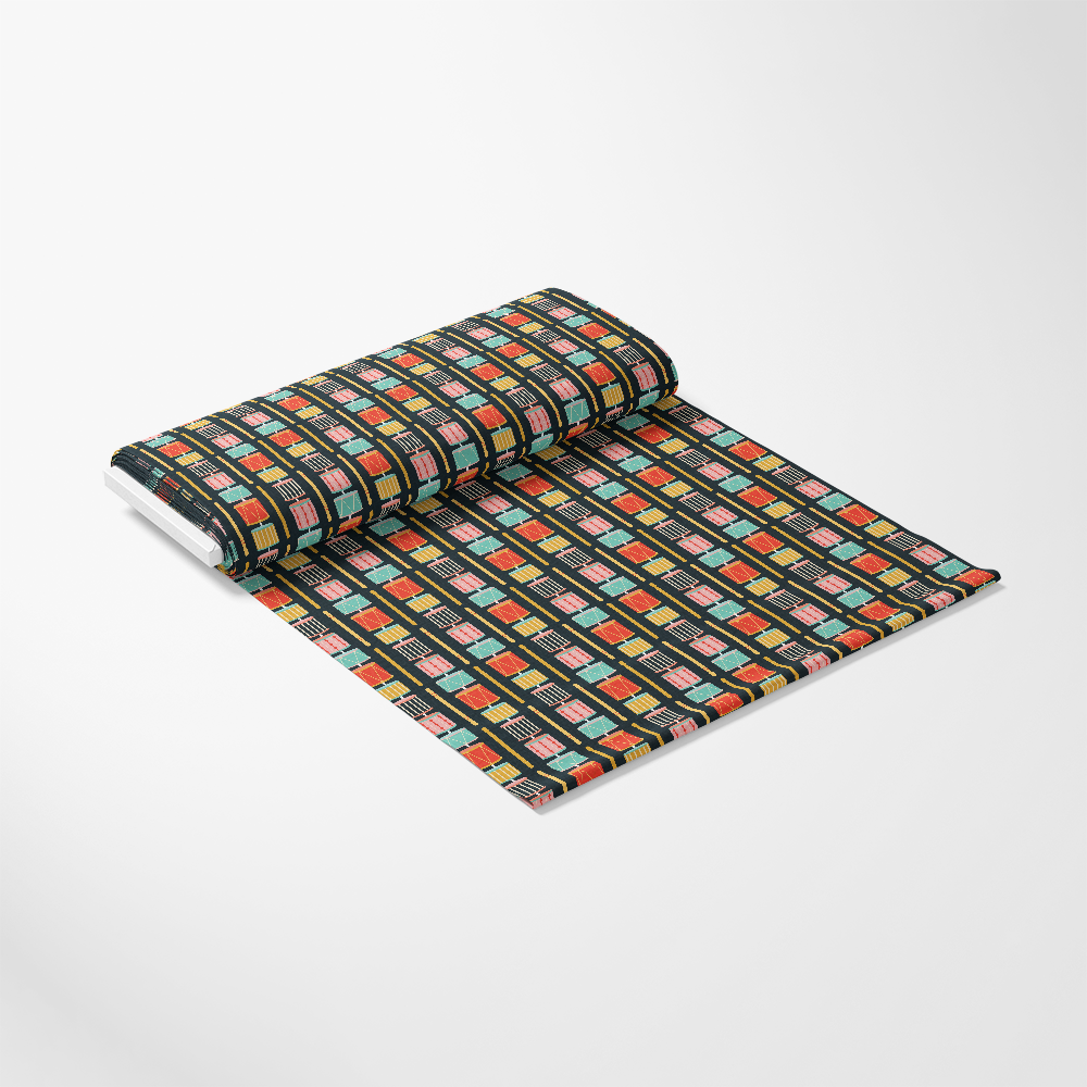 A roll of fabric with a pattern of colorful geometric shapes, mainly rectangles and squares, unrolled on a white surface.