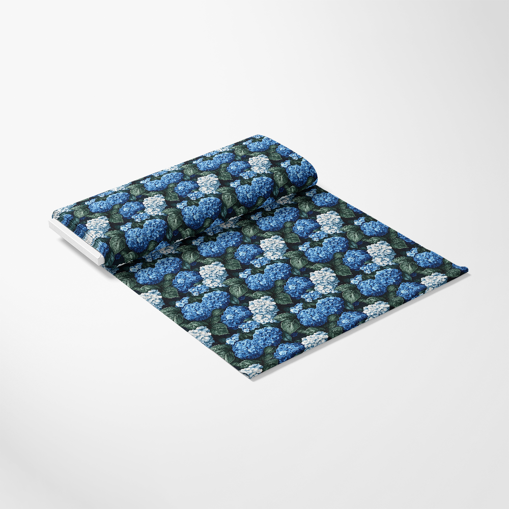 A roll of fabric featuring a pattern of blue and white hydrangea flowers against a dark background on a plain surface.