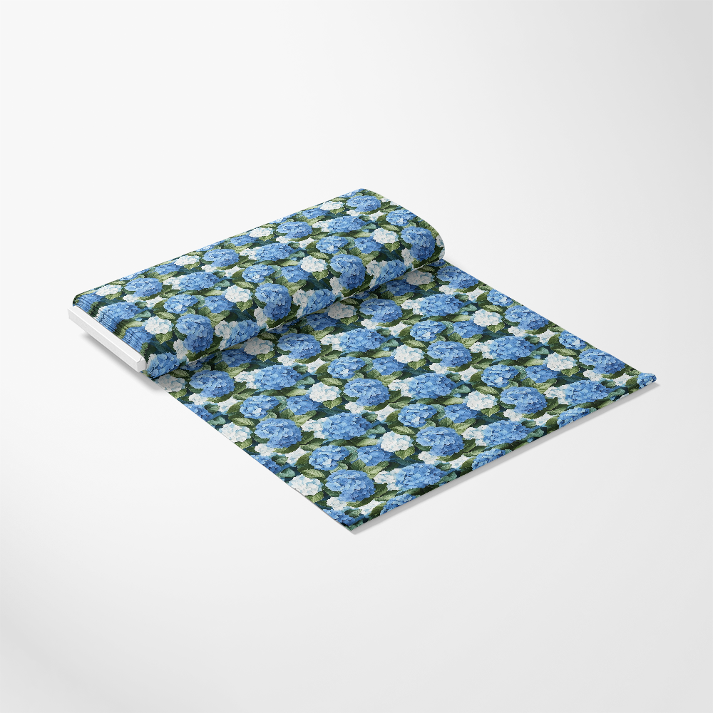 A roll of fabric with a pattern of blue and white flowers on a green background is partially unrolled on a white surface.