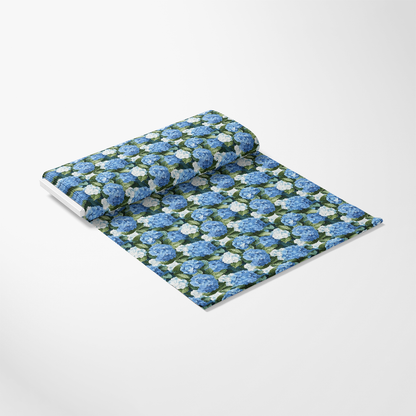 A roll of fabric with a pattern of blue and white flowers on a green background is partially unrolled on a white surface.