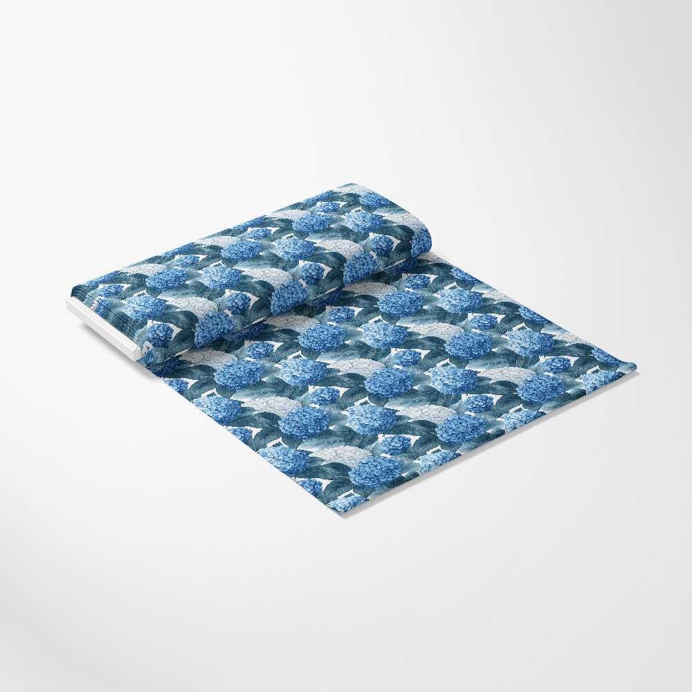 A roll of wallpaper featuring a pattern of blue hydrangeas with green leaves on a light background, partially unrolled and lying flat.