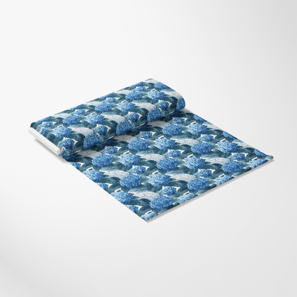A roll of wallpaper featuring a pattern of blue hydrangeas with green leaves on a light background, partially unrolled and lying flat.