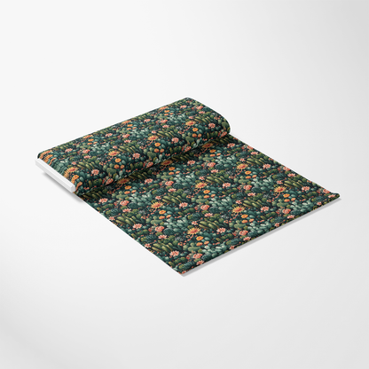 A rolled-out sheet of dark floral wallpaper with colorful, small flowers and green leaves on a white surface.