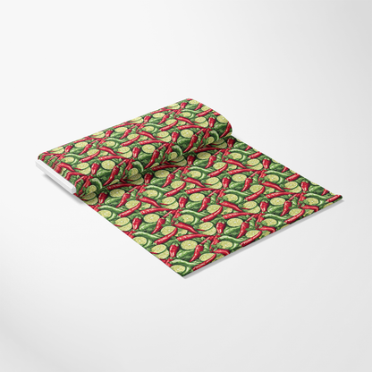A roll of fabric lies partially unrolled, displaying a pattern of red peppers and green geometric shapes against a white background.