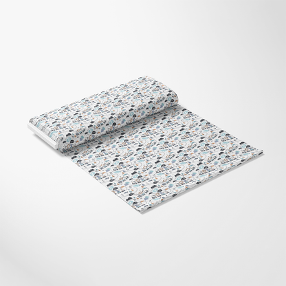 A roll of patterned wrapping paper is partially unrolled on a white surface. The paper features a repeated design with various vehicles and travel-themed icons in blue, gray, and beige tones.