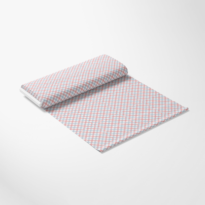 A roll of fabric unrolled on a flat surface, featuring a checkered pattern in pink, blue, and white colors. The background is plain and white.