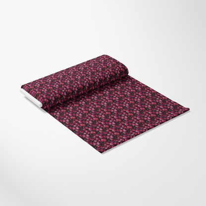 A roll of fabric with a black background and a pattern of small red and pink flowers, displayed partially unrolled on a plain surface.