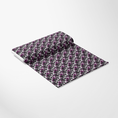 A roll of fabric partially unrolled, featuring a repeating floral pattern in shades of purple and white on a black background, displayed on a plain white surface.