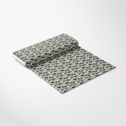 A roll of fabric partially unrolled on a white surface, featuring a repeating black and gray floral pattern.