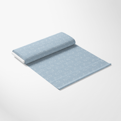A roll of light blue fabric with a subtle white floral pattern is partially unrolled on a plain white surface.