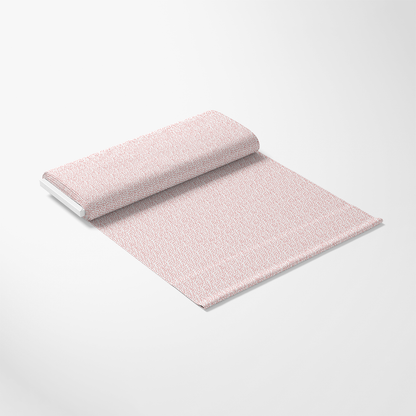 A roll of light-colored fabric with a subtle, small-scale pink and white pattern is partially unrolled on a plain white surface. The fabric appears smooth and neatly arranged.