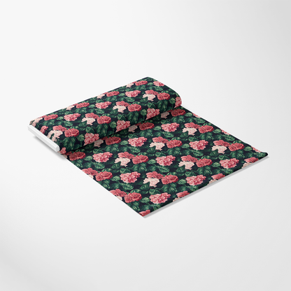 A roll of fabric with a floral pattern featuring pink roses and green leaves on a dark background, partially unrolled with the pattern visible.