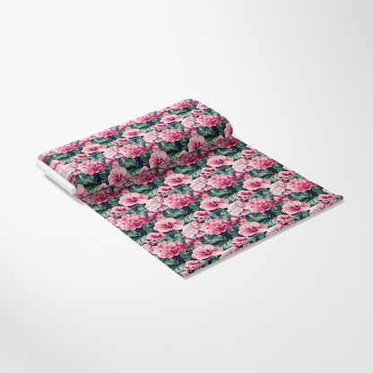 A roll of patterned fabric with pink flowers and green leaves on a white background, unrolled slightly to display the design.