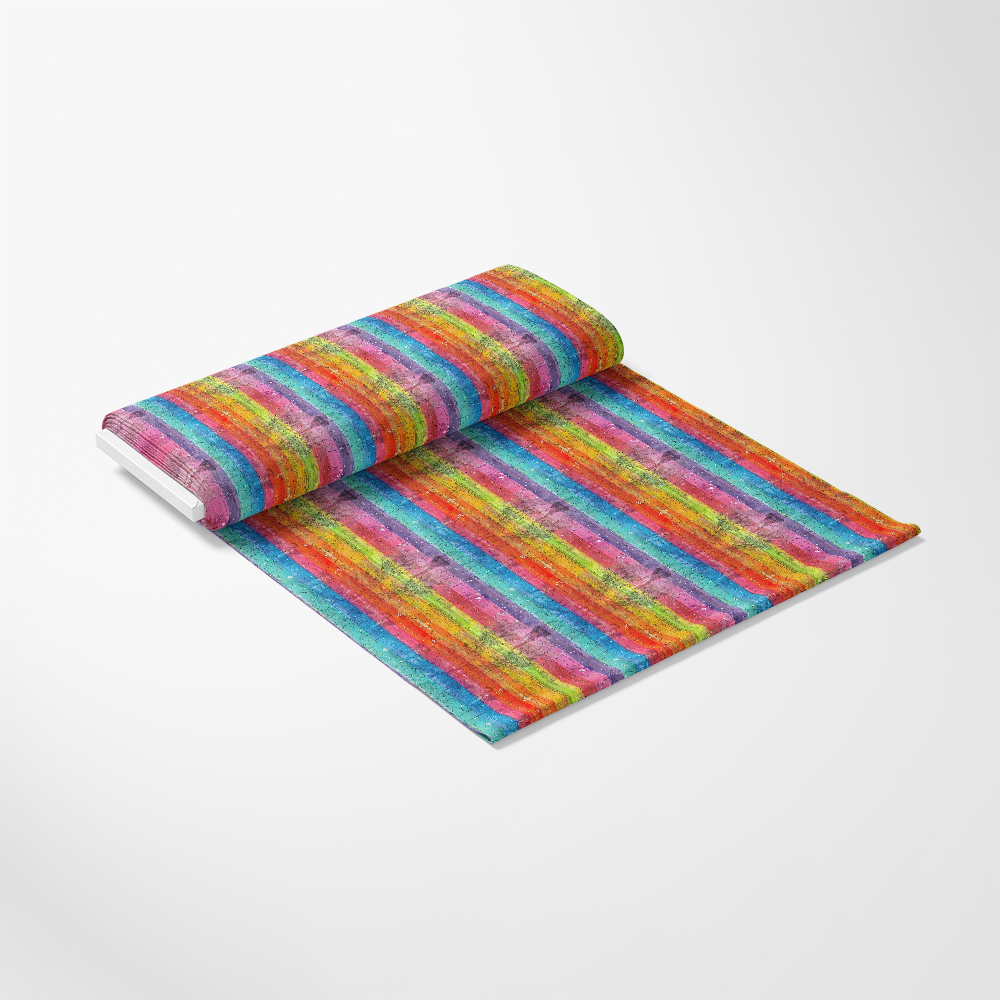 A roll of fabric unrolled on a flat surface, featuring a colorful, horizontal striped pattern in shades of red, orange, yellow, green, blue, and purple, set against a plain white background.