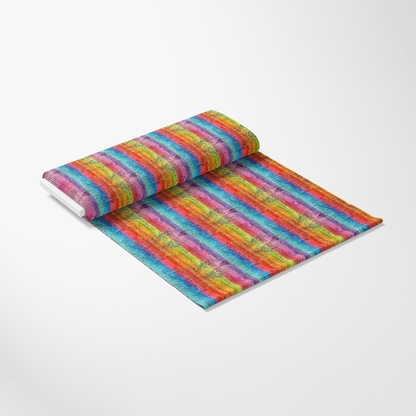 A roll of fabric unrolled on a flat surface, featuring a colorful, horizontal striped pattern in shades of red, orange, yellow, green, blue, and purple, set against a plain white background.