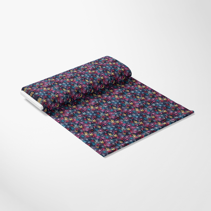 A roll of fabric partially unrolled on a flat surface, displaying a colorful, abstract floral pattern against a dark background. The fabric is arranged diagonally with the roll on the upper left side.