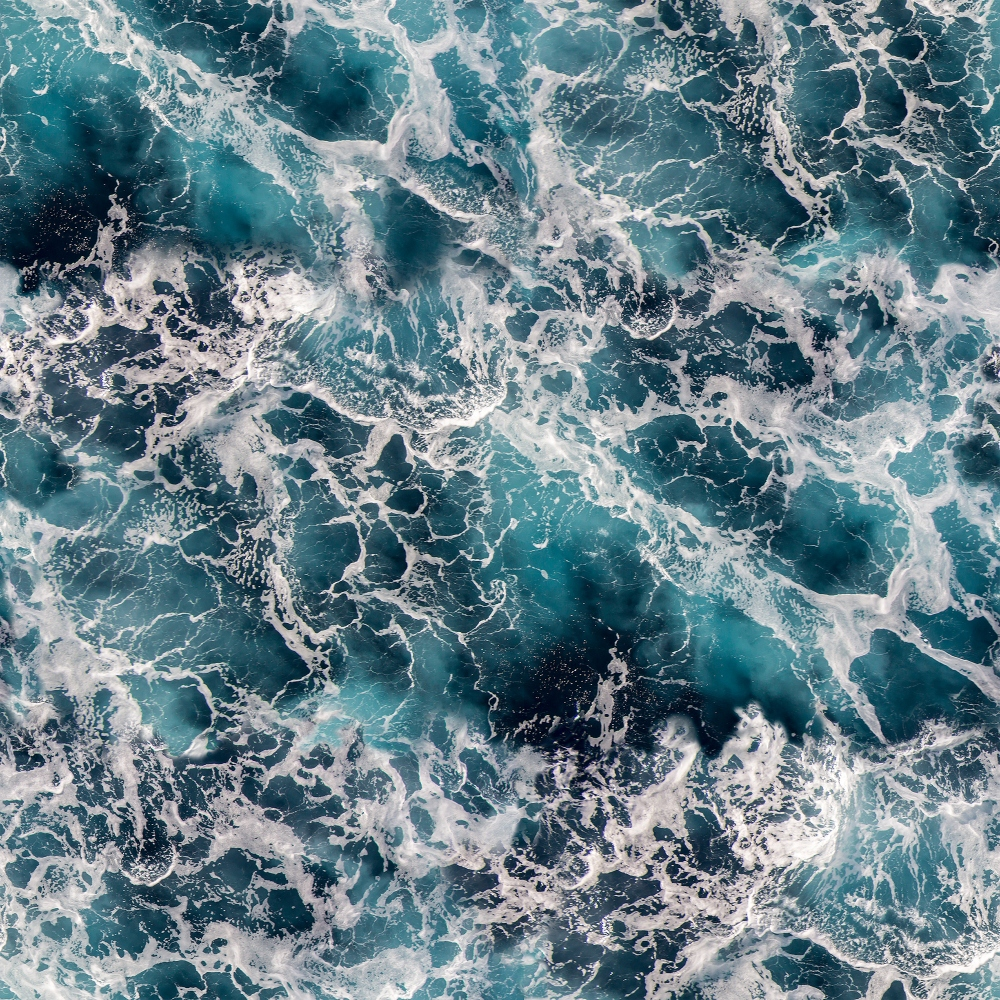 Aerial view of turbulent ocean waves creating a pattern of white foam against the deep blue water surface.