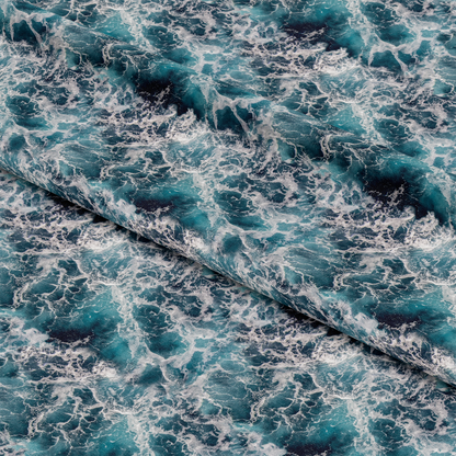 Close-up of fabric with a turbulent ocean wave pattern in shades of blue and white. The fabric is folded diagonally, displaying the dynamic, swirling design.