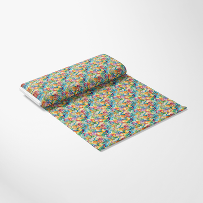 A roll of patterned wrapping paper with a colorful, repetitive design featuring various cartoon-style fruits, unrolled onto a white surface. The background is plain and well lit.