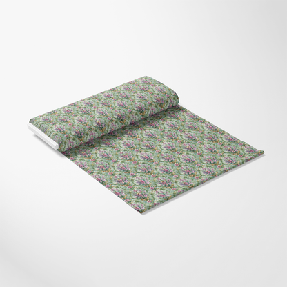 A roll of wallpaper partially unrolled on a white surface, featuring a green background with a repeating floral pattern in pink, purple, and green tones.
